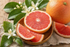 Frisches Duftbild mit rosa Grapefruit, Grapefruitscheiben und grünen Blättern auf natürlichem Hintergrund für ätherisches Grapefruitöl