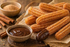Warmes Duftbild mit Churros, Zimt-Zucker und Schokoladensauce auf rustikalem Hintergrund für Churros Fragrance Oil