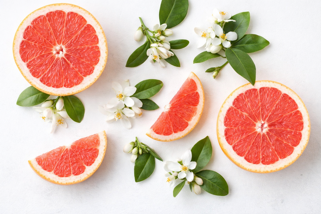 Frische pinke Grapefruitstücke und weiße Blüten auf hellem Hintergrund als Duftbild für ein fruchtig-zitrisches Parfümöl.

