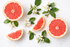 Frische pinke Grapefruitstücke und weiße Blüten auf hellem Hintergrund als Duftbild für ein fruchtig-zitrisches Parfümöl.

